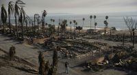 A person walks past damage from the Palisades Fire on Friday, Jan. 10, 2025, in the Pacific Palisades section of Los Angeles. (AP Photo/John Locher)