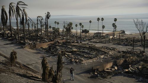 A person walks past damage from the Palisades Fire on Friday, Jan. 10, 2025, in the Pacific Palisades section of Los Angeles. (AP Photo/John Locher)