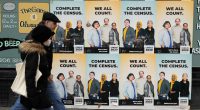 FILE - People walk past posters encouraging participation in the 2020 Census in Seattle