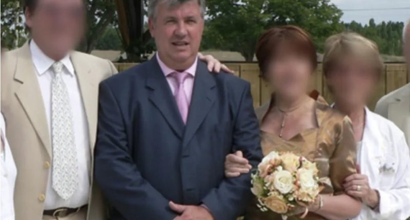 Man in a suit at a wedding with blurred faces of other attendees.