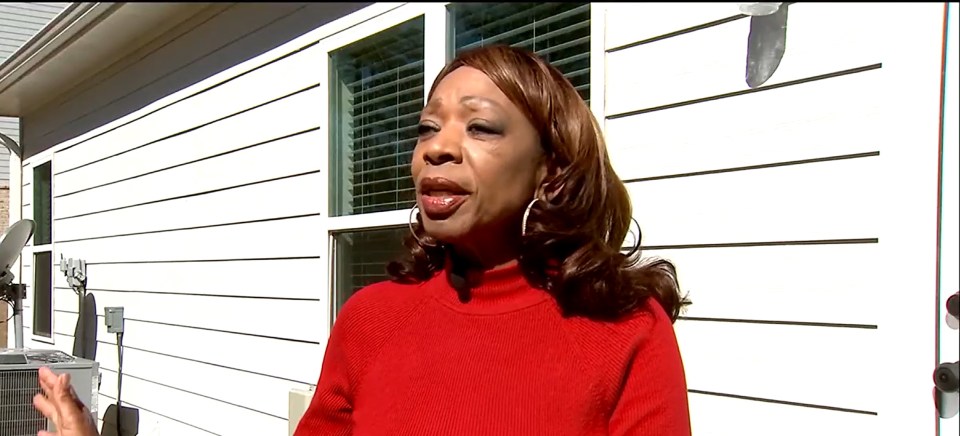 Woman in red sweater speaking outside a house.