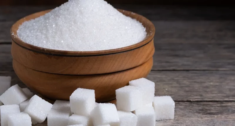 Granulated sugar in a wooden cup, a scattering of refined sugar cubes