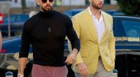 Two men walking outdoors, one in a yellow blazer and the other in a black turtleneck.