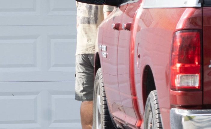Man standing by red truck in front of garage.