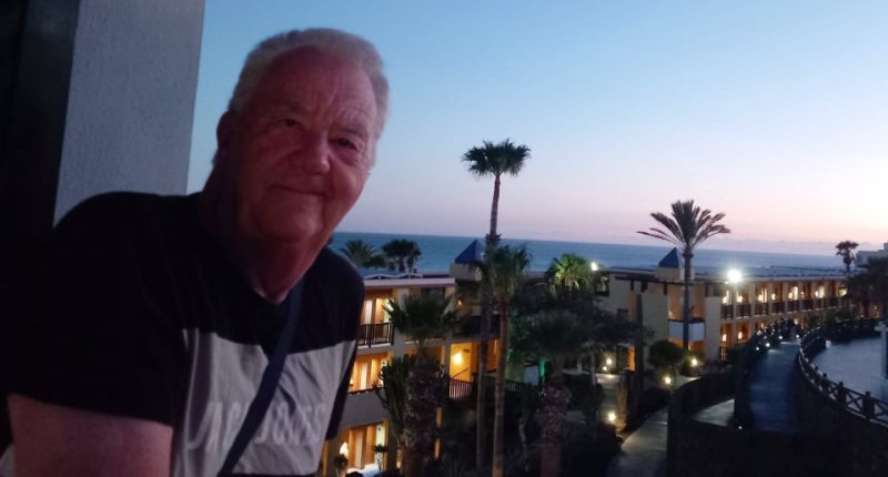 A man on a balcony overlooking a resort at dusk.