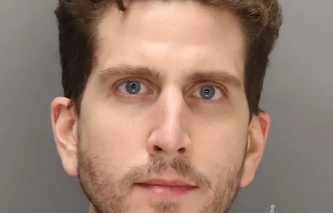 Mugshot of a man with curly brown hair and a beard.