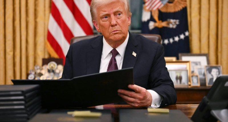 Donald Trump reviewing documents at his desk in the Oval Office.