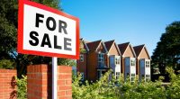 House for sale sign in front of a row of houses.
