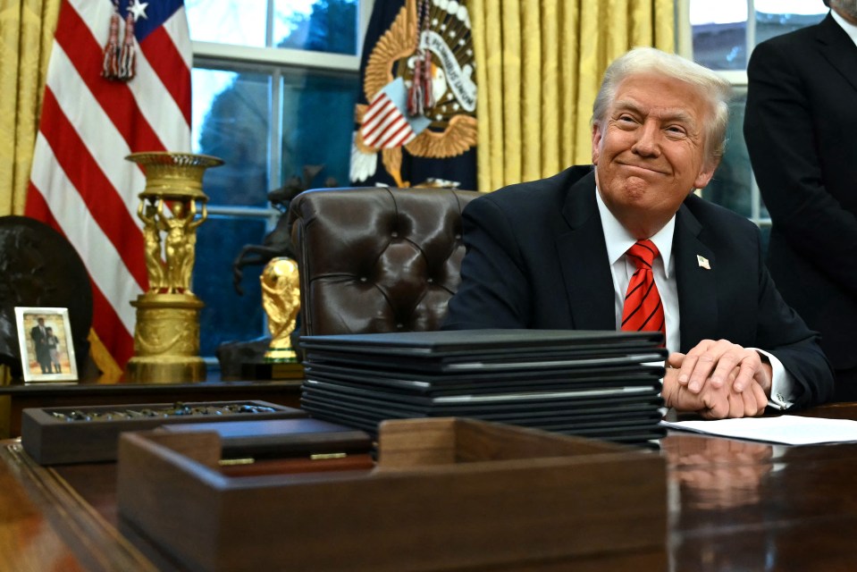 Donald Trump smiling at his desk in the Oval Office.