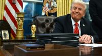 Donald Trump smiling at his desk in the Oval Office.