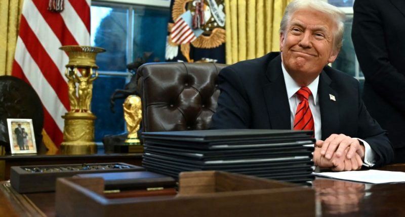 Donald Trump smiling at his desk in the Oval Office.