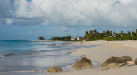 Beach scene with turquoise water, white sand, palm trees, and a building in the distance.