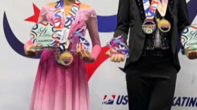 Two young figure skaters holding medals and trophies.