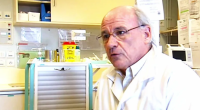 A doctor in a white coat speaks in a hospital room.