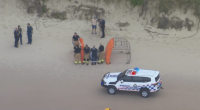 Emergency responders attending to a person on a beach.