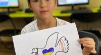 Girl holding drawing of dove carrying Ukrainian flag.