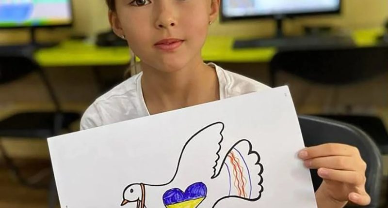 Girl holding drawing of dove carrying Ukrainian flag.