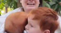 A woman holding two young children, crying.