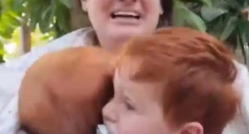 A woman holding two young children, crying.