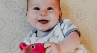 Smiling baby holding a pink stuffed animal.