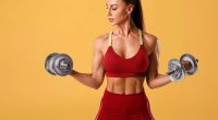 fit woman holding dumbbells in front of yellow background, concept of dumbbell workout for abs in 30 days