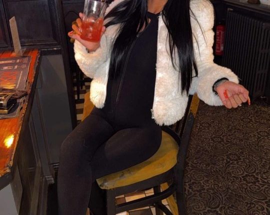 A woman sitting on a bar stool, holding a drink.