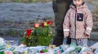 A young girl stands near a memorial of flowers and candles.