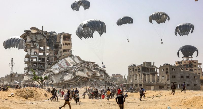 People rush to collect humanitarian aid packages dropped by parachute in a war-torn area.
