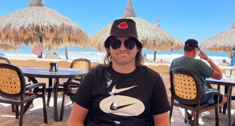 Man sitting at an outdoor restaurant table by the beach.