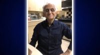 Man in a dark blue shirt sitting in his kitchen.