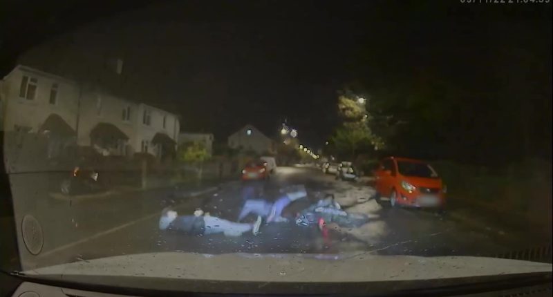 Screengrab of a police car hitting a motorbike, causing the driver and passenger to fall.