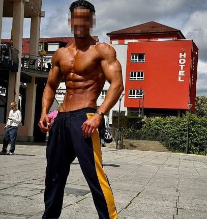 Muscular man in sweatpants standing in front of a hotel.