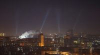 Nighttime view of Kyiv, Ukraine, with searchlights scanning the sky during a drone strike.