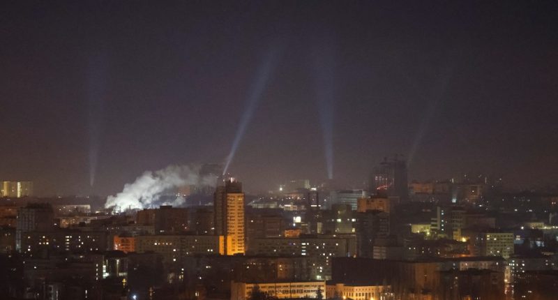 Nighttime view of Kyiv, Ukraine, with searchlights scanning the sky during a drone strike.