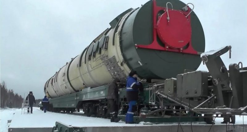 a man in a blue jacket stands next to a train with a large tank on it