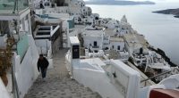 Person descending stairs in Santorini, Greece, with whitewashed buildings and ocean view.