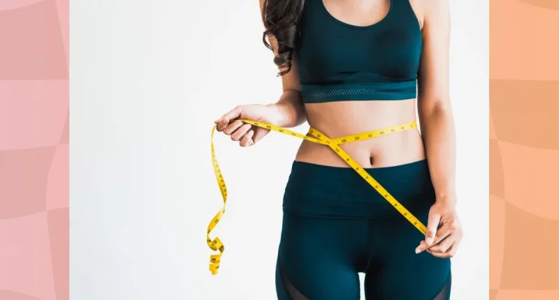 close-up of woman in workout clothes measuring her waistline with tape measure