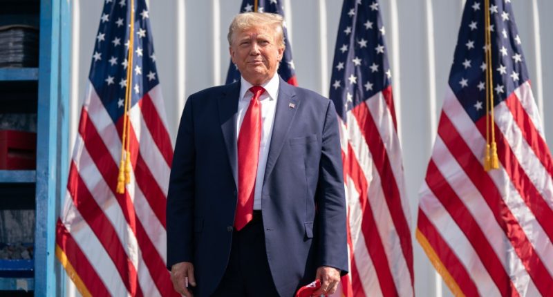 Donald Trump standing in front of American flags.