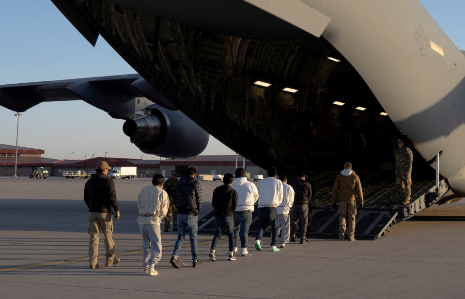Detained migrants being escorted onto a military aircraft.