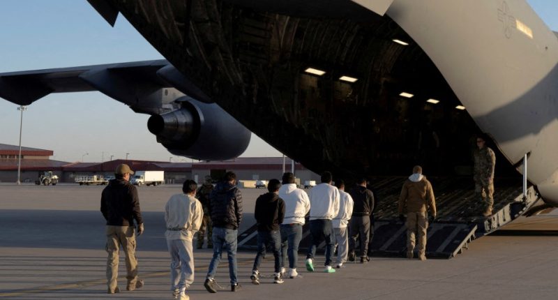 Detained migrants being escorted onto a military aircraft.