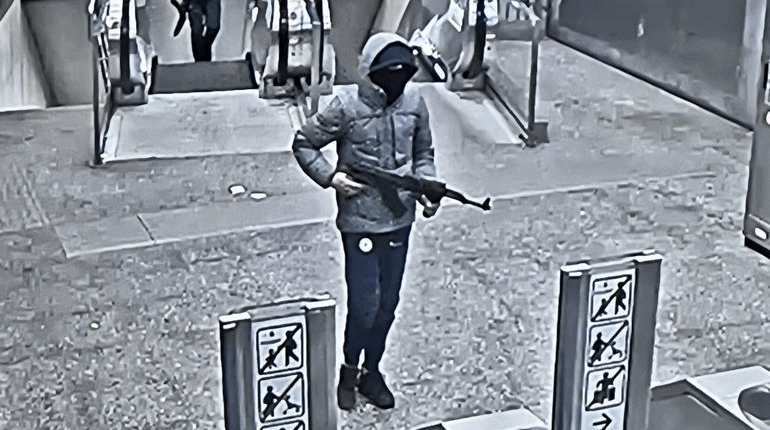 Surveillance image of a suspect holding an assault rifle at a train station.