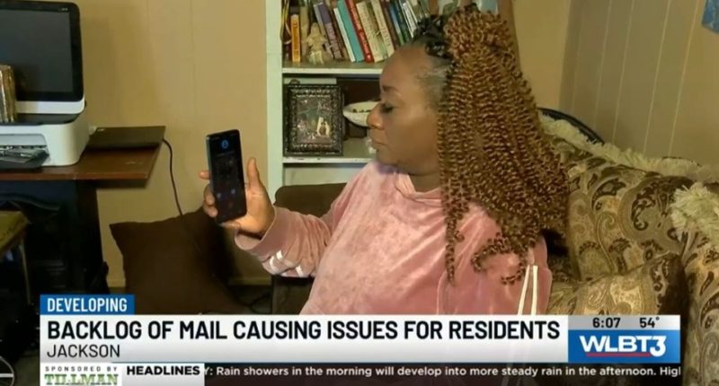 Woman showing phone screen; news report about mail backlog.