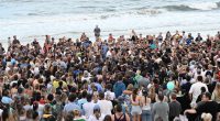 A large group of people gathered on a beach for a vigil.