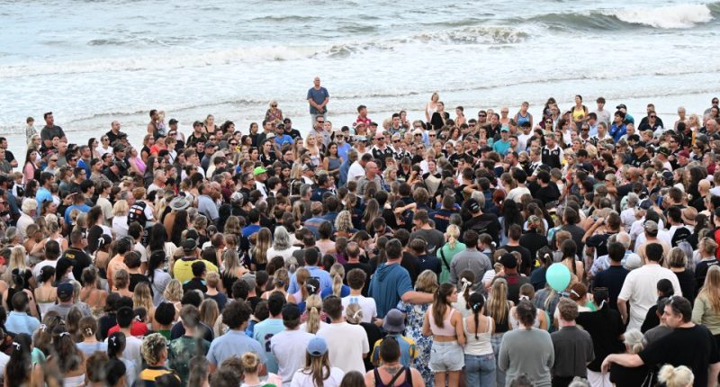 A large group of people gathered on a beach for a vigil.
