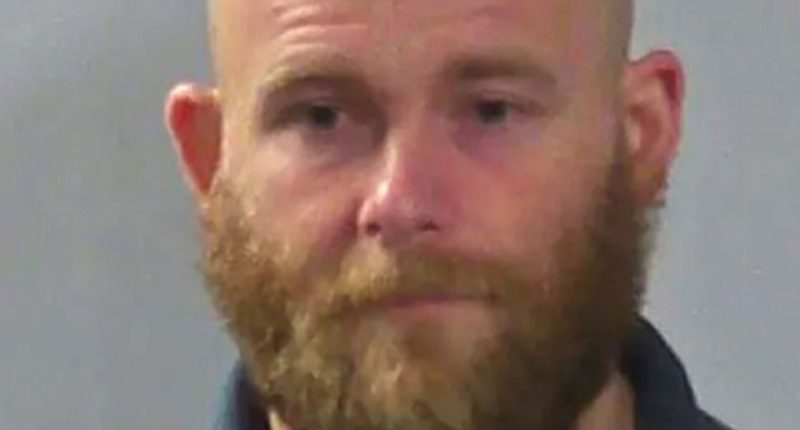 Mugshot of a balding man with a reddish beard.