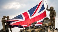 British soldiers raising the Union Jack flag on a military vehicle.