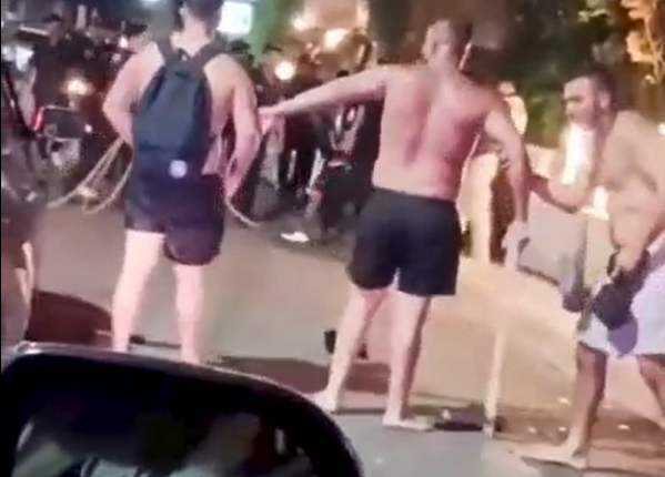 Three shirtless men arguing on a street at night.