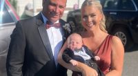 A man and woman in formal attire holding a baby dressed in a tuxedo.