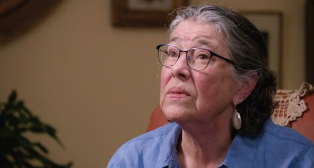 A woman wearing glasses looks thoughtfully off to the side.