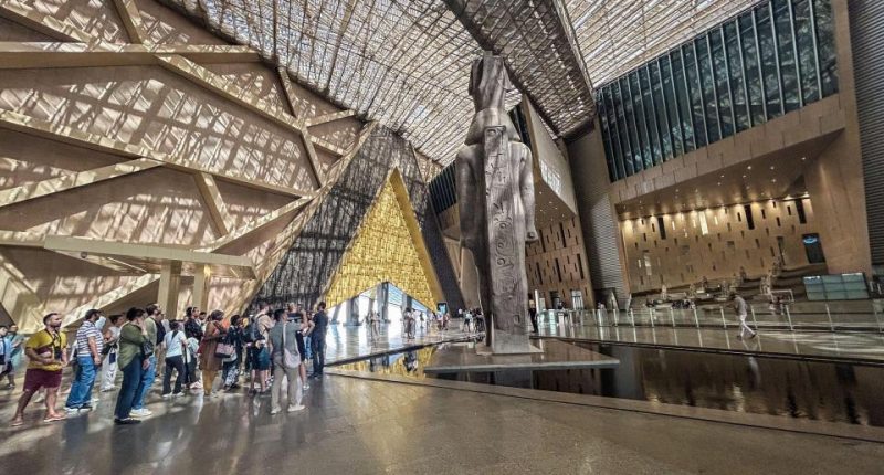 Grand Egyptian Museum interior with a large statue and visitors.